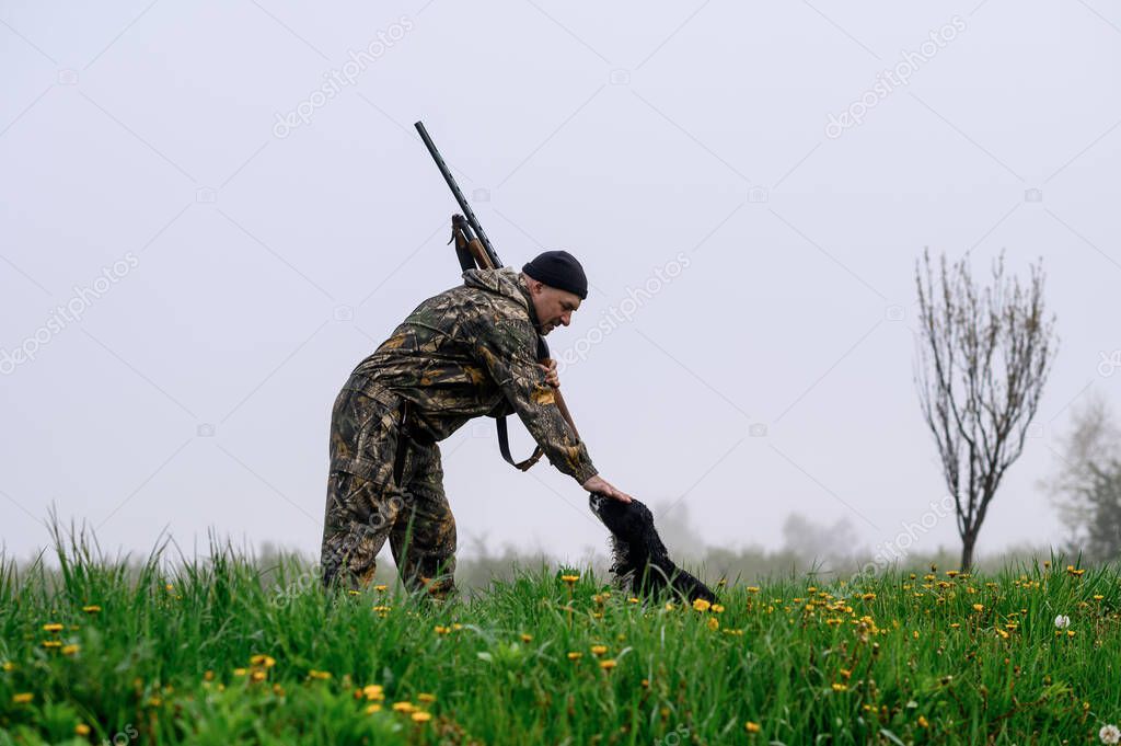 Male hunter with a gun on his shoulder stroking a dog Russian spaniel in a fogg