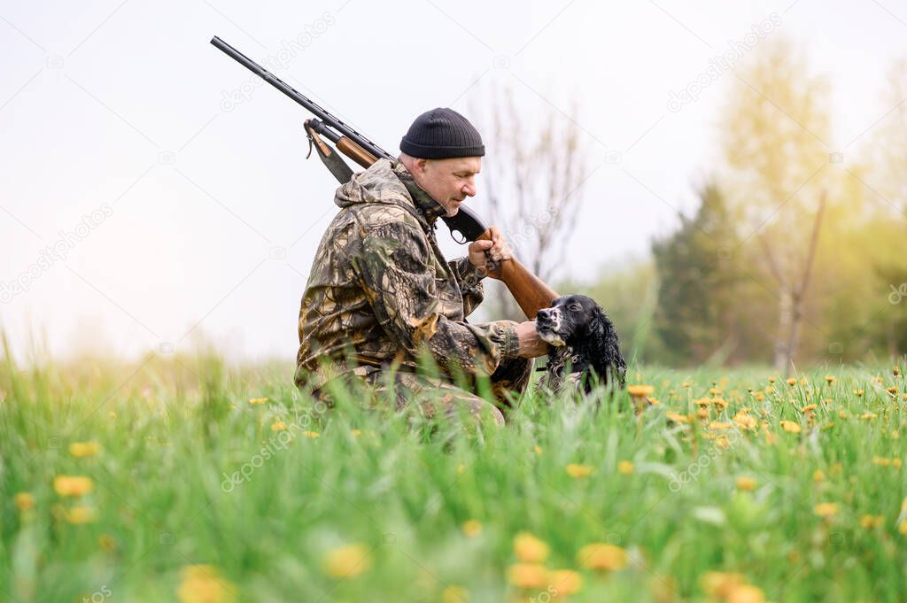 Male hunter with a gun on his shoulder stroking a dog Russian spaniel