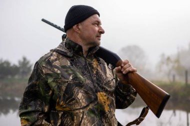 Avcı omzunda silahla sisli bir gölün arka planında