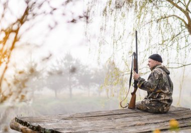 Erkek avcı, gün doğumu ve gölün arka planında bir köprüde oturuyor.