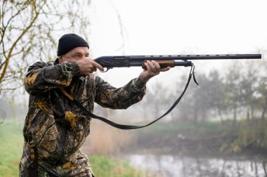 Silahlı bir avcı köpeği Rus Spaniel ile köprüye nişan alıyor.