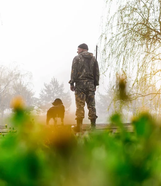 Hunter with a gun stands on the bridge with his dog Russian Spaniel — Stockfoto