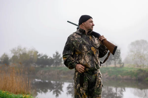 Hunter with a gun on his shoulder on a background of misty morning lake — Stockfoto