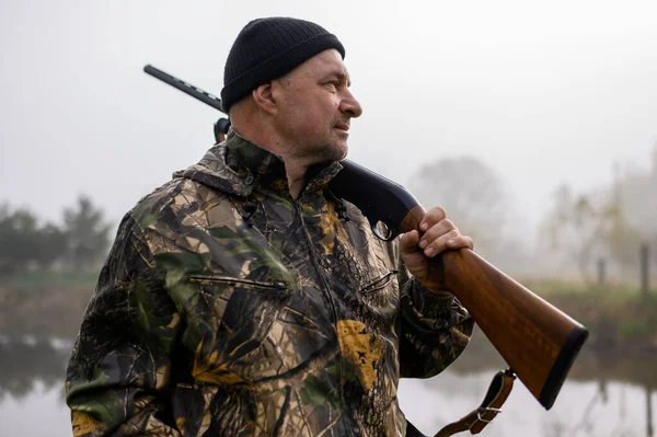 Avcı omzunda silahla sisli bir gölün arka planında