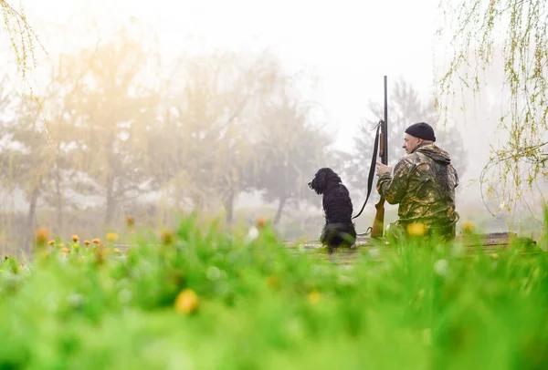 Männlicher Jäger sitzt mit einem russischen Spaniel auf einer Brücke — Stockfoto