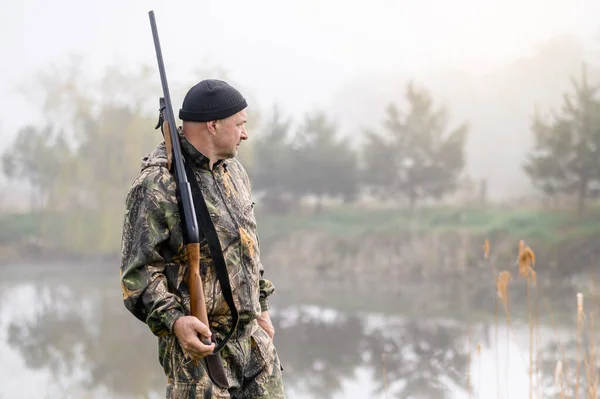 Hunter with a gun on his shoulder on a background of misty morning lake — Stockfoto