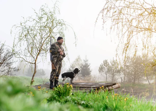 Jäger mit Waffe steht mit seinem Hund Russian Spaniel auf der Brücke — Stockfoto
