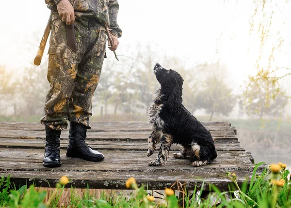 Jäger hobelt einen Ast mit einem Messer auf den Hintergrund eines Hundes und einer Brücke — Stockfoto