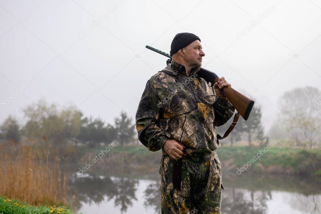 Hunter with a gun on his shoulder on a background of misty morning lake