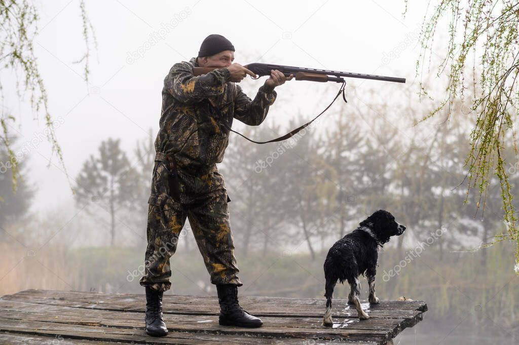 Hunter with a gun aims at the bridge with his dog Russian Spaniel