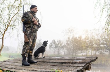 Silahlı avcı köpeği Rus Spaniel ile köprüde duruyor.