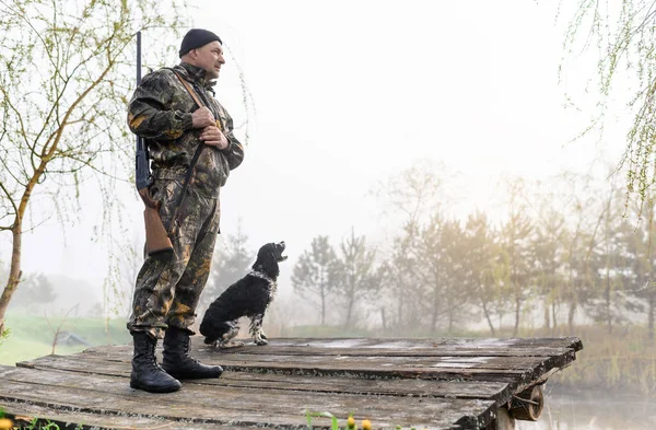 Silahlı avcı köpeği Rus Spaniel ile köprüde duruyor.
