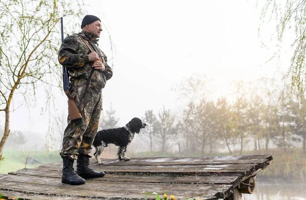 Silahlı avcı köpeği Rus Spaniel ile köprüde duruyor.
