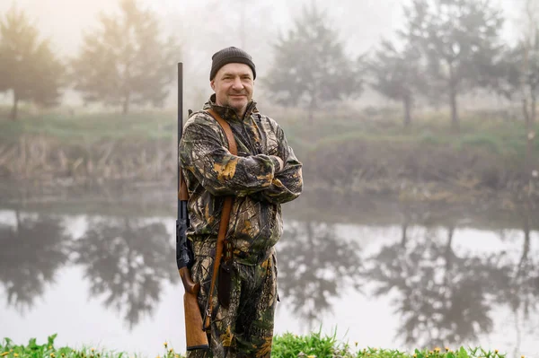 Omzunda silah olan yakışıklı bir adam sisli göle bakıyor.