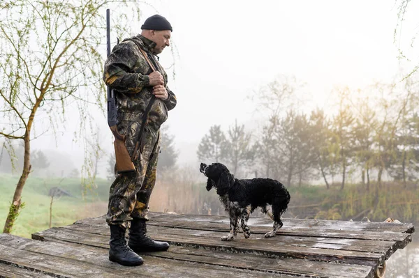 Jäger mit Waffe steht mit seinem Hund Russian Spaniel auf der Brücke — Stockfoto