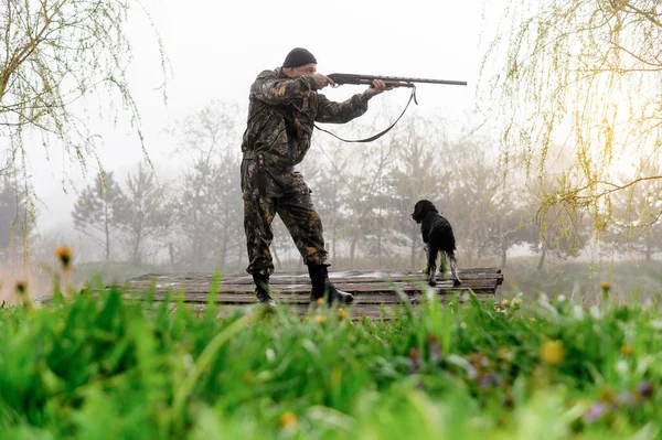 Hunter with a gun aims at the bridge with his dog Russian Spaniel — Stockfoto