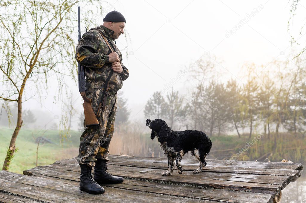 Hunter with a gun stands on the bridge with his dog Russian Spaniel
