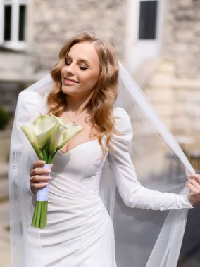 Beyaz elbiseli güzel sarışın gelin peçesiyle oynuyor.