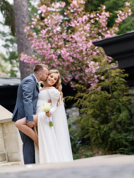 Bonito casal caucasiano recém-casado beijando no fundo da sakura — Fotografia de Stock