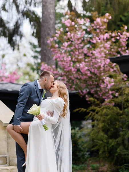 Beautiful newlywed caucasian couple kissing on the background of sakura — Stock fotografie