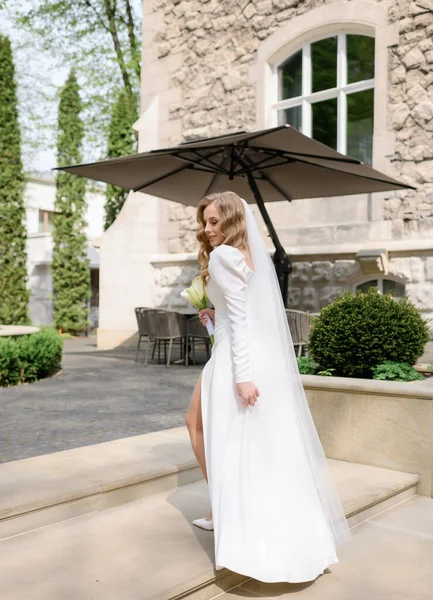 Beautiful blonde caucasian bride in a white dress with a slit posing — Stok fotoğraf