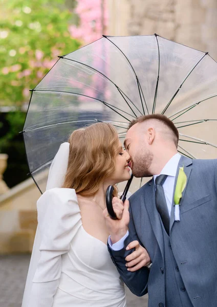 Belo casal recém-casado caucasiano com poses de guarda-chuva transparentes e abraços — Fotografia de Stock