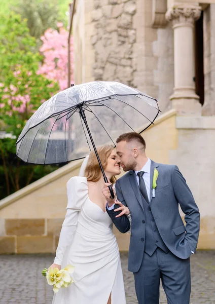 Belo casal recém-casado caucasiano com poses de guarda-chuva transparentes e abraços — Fotografia de Stock