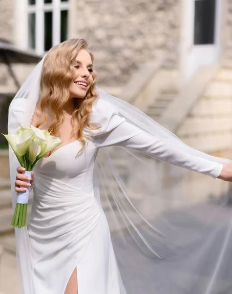 Красивая блондинка невеста в белом платье играет с ее вуали — стоковое фото