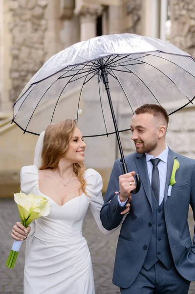 Belo casal recém-casado caucasiano com poses de guarda-chuva transparentes e abraços — Fotografia de Stock