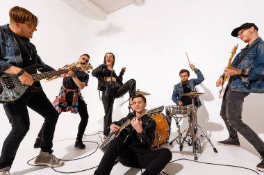 Beyaz bir arka planda altı kişilik genç bir rock grubu çalıp şarkı söylüyor.