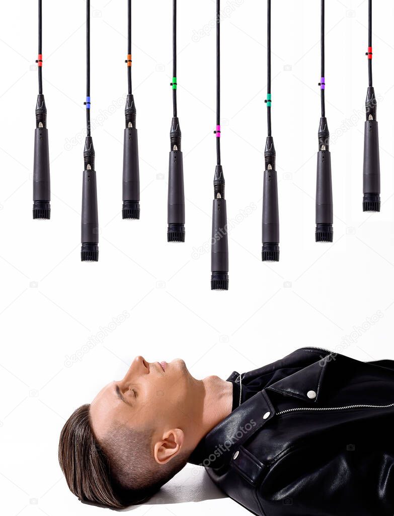 Young caucasian guy lying on white floor above him hanging many microphones