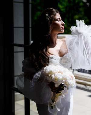 Beyaz elbiseli beyaz elbiseli güzel, beyaz şakayık desenli bir gelin. Siyah arka planda, güneşte poz veriyor. Kapat.