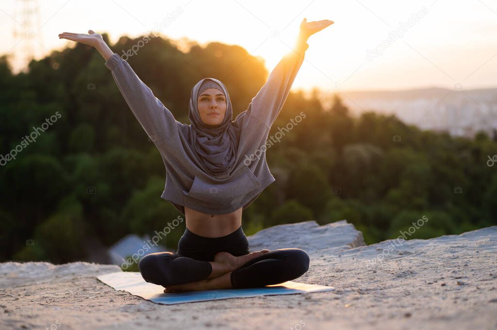 Beautiful young girl in a hijab meditates on a background of sunset and landscape. The concept of a healthy lifestyle