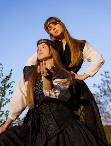 Portrait of a couple of beautiful young Caucasian girls in traditional Ukrainian national clothes posing stylishly at sunset in the mountains