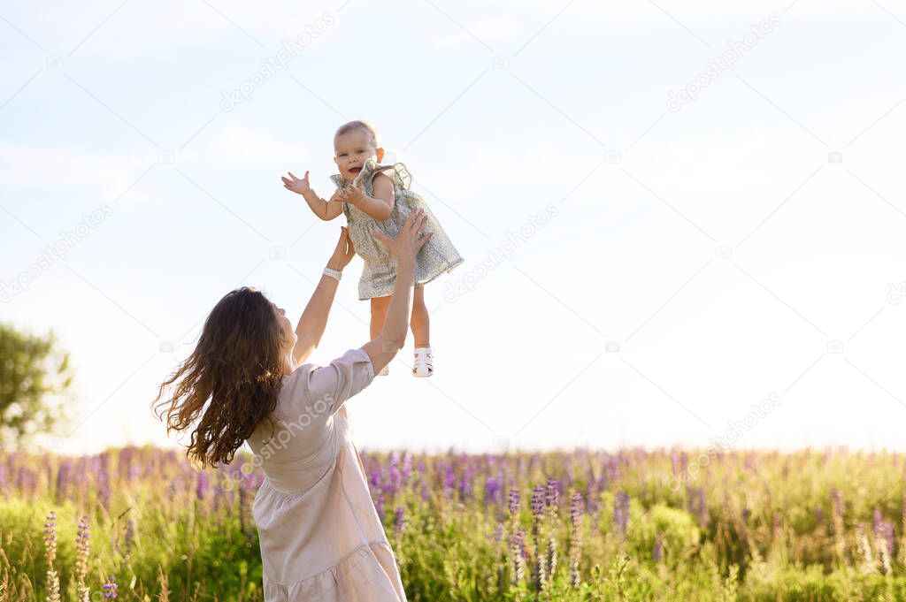 Beautiful young Caucasian mother with a little girl in her arms on the background of the sunset in a field of lupine flowers are hugging