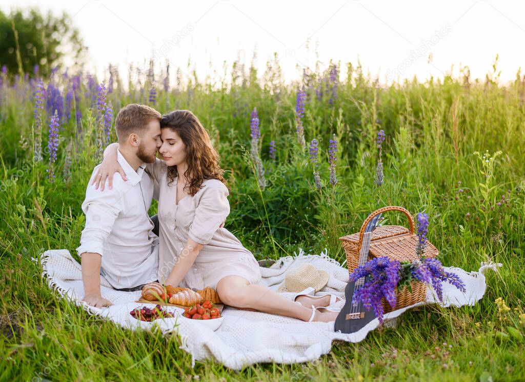 Young beautiful Caucasian family boy and girl posing on a picnic against the background of the sunset in a field of lupines