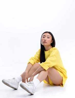 Beautiful Asian girl in a yellow linen casual suit posing against a white wall in a photo studio