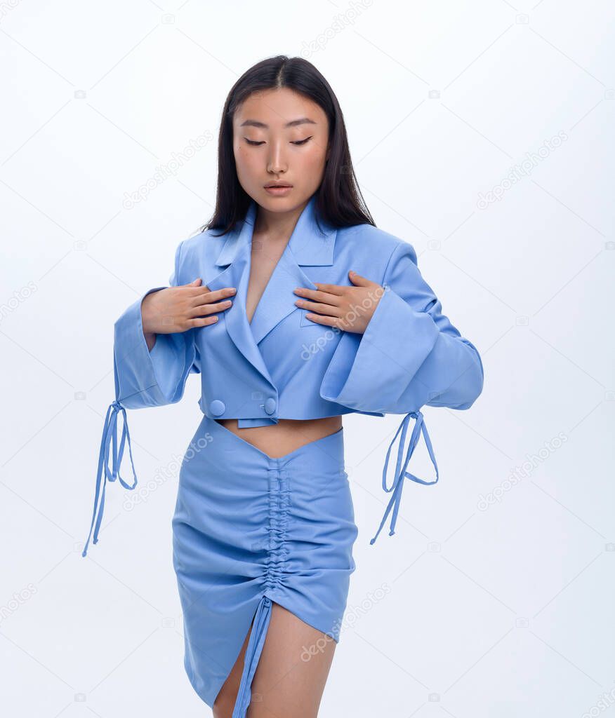 A beautiful Asian girl in a blue suit poses against a white wall in a photo studio