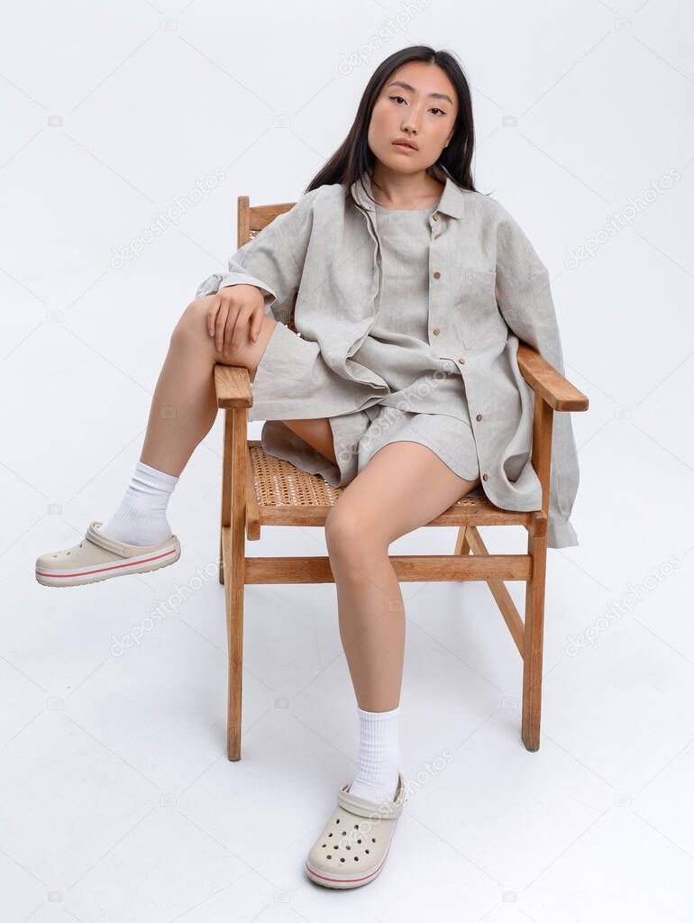 Beautiful Asian girl in a gray linen casual suit posing against a white wall in a photo studio