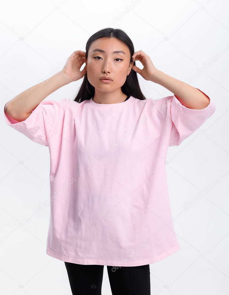 Beautiful Asian girl in a pink t-shirt posing against a white wall in a photo studio