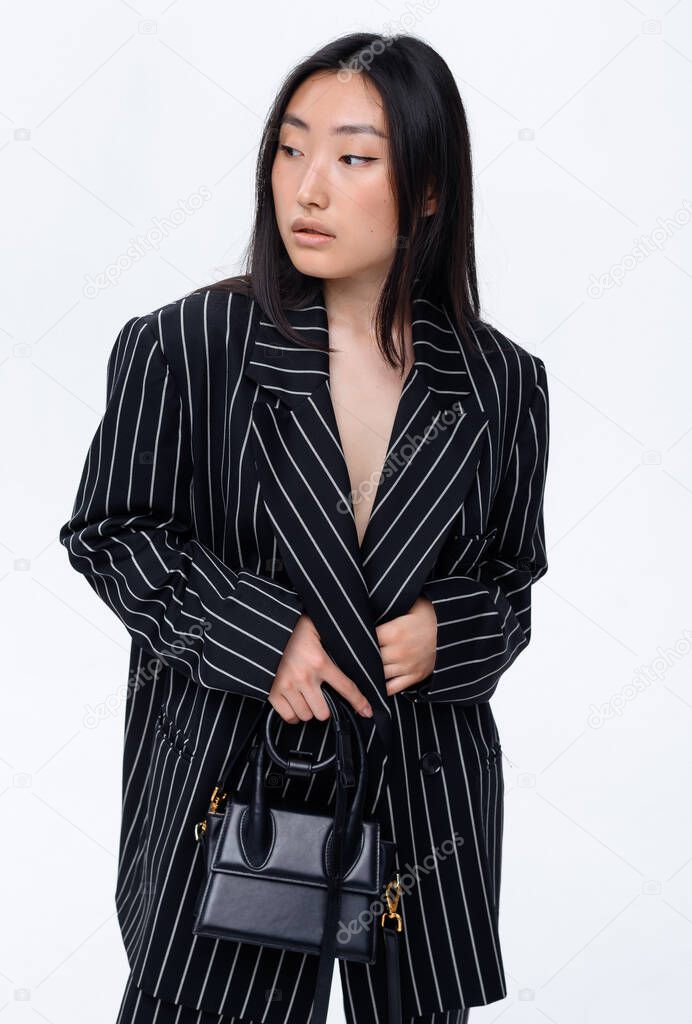 Beautiful Asian brunette girl in a stylish black fashion suit posing on a white background