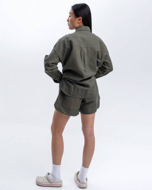 Yeşil keten takım elbiseli güzel bir Asyalı kız fotoğraf stüdyosunda beyaz bir duvara poz veriyor.