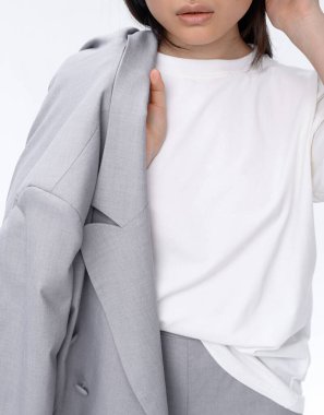 Gri takım elbiseli güzel bir Asyalı kız fotoğraf stüdyosunda beyaz bir duvara karşı poz veriyor. Moda çekimi.