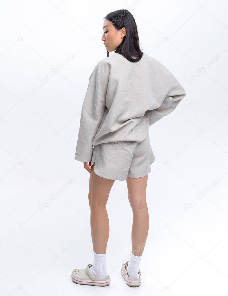 Beautiful Asian girl in a gray linen casual suit posing against a white wall in a photo studio