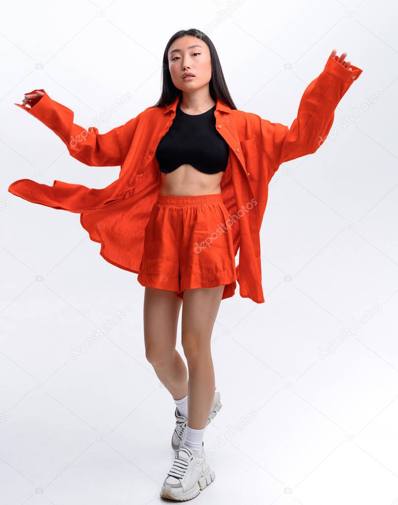 Beautiful Asian girl in orange linen casual suit posing against white wall in photo studio