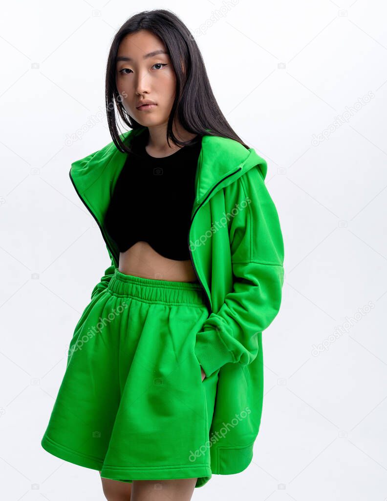 Beautiful Asian girl in a green sports suit casual posing against a white wall in a photo studio