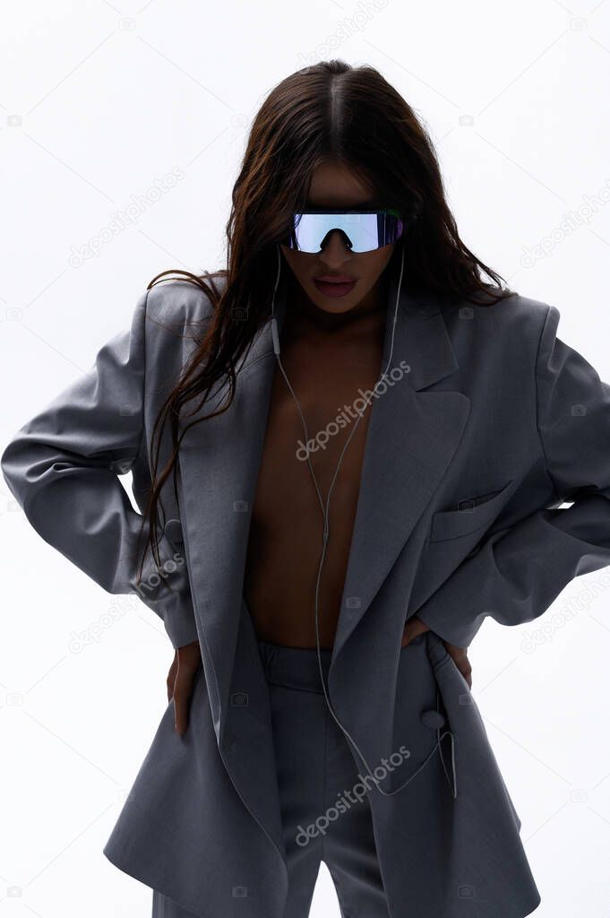 Beautiful Caucasian brunette girl in stylish glasses in a gray fashion suit posing on a white background in headphones