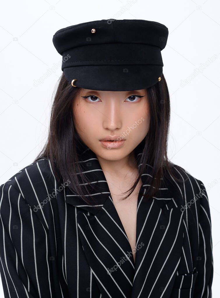 Beautiful Asian brunette girl in a stylish hat in a black fashion suit posing on a white background