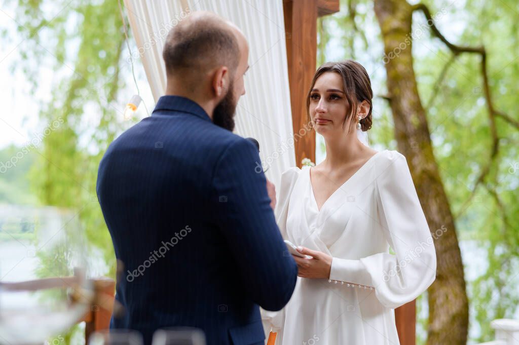 A beautiful couple of newlyweds make marriage promises against the background of the wedding arch ceremony in the forest
