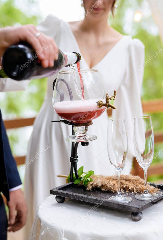 A beautiful newlywed couple pours champagne into a vessel. Close-up